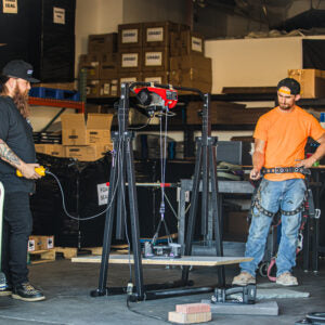 GRABO GR-V1 wireless remote demonstrated by two operators beside a workshop hoist. Application photo; hoist and lifters not included.